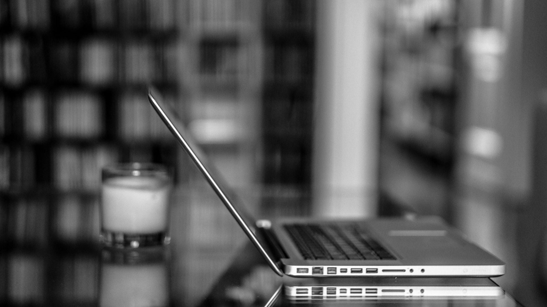 Black and white picture of a home office with a candle and laptop on the table