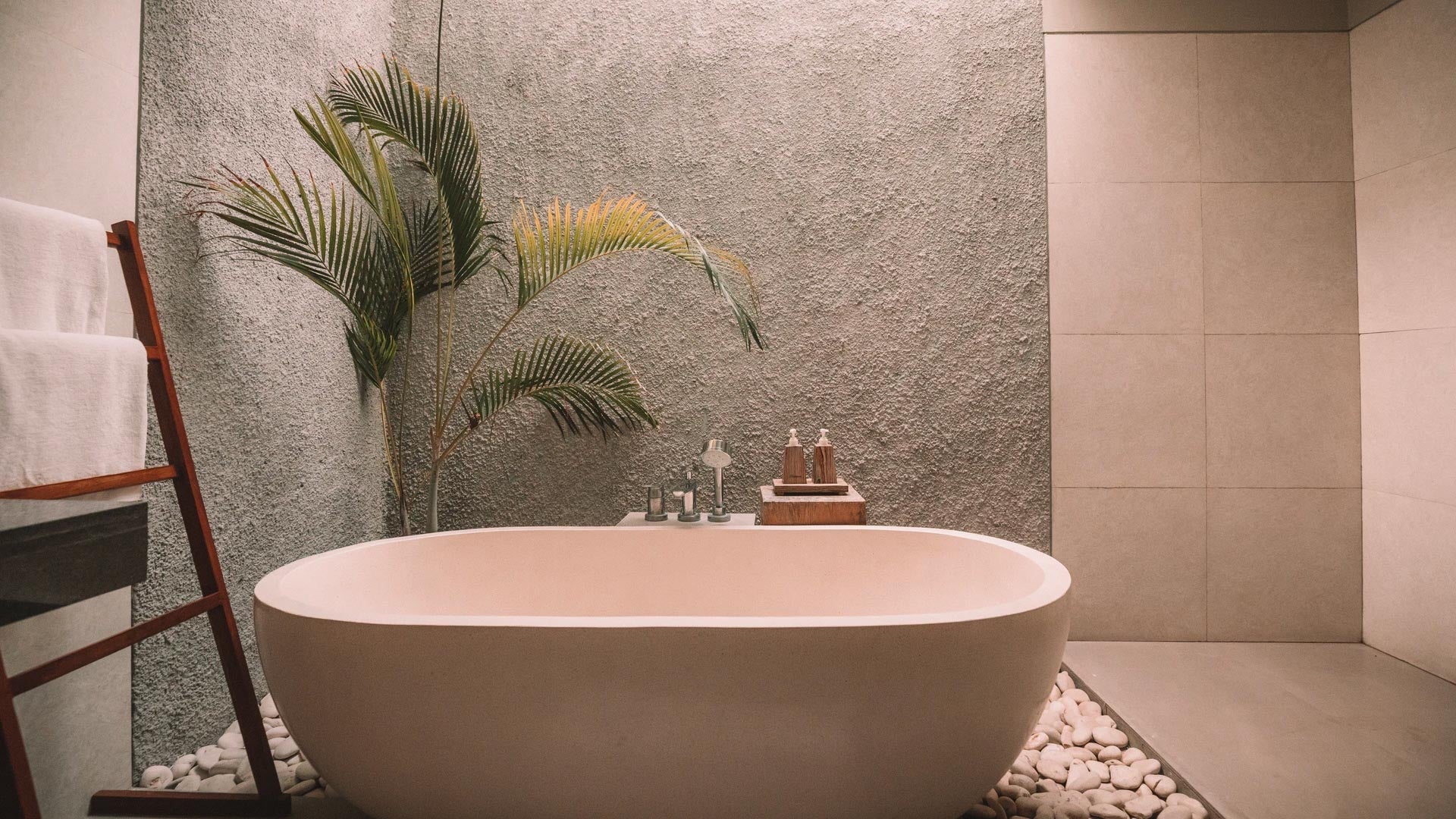 A free-standing spa bath surrounded by pebbles and a palm tree