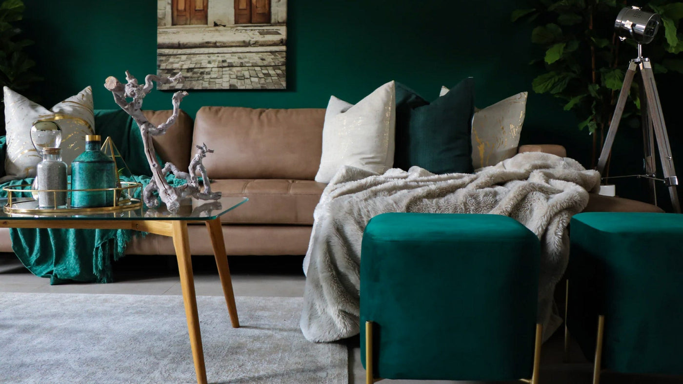 A cosy living room with green walls, a green couch, cushions and blankets