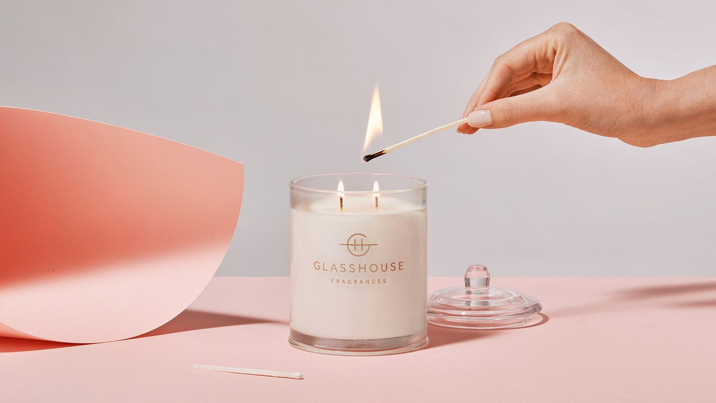 A woman's hand lighting a Glasshouse candle on a pale pink table