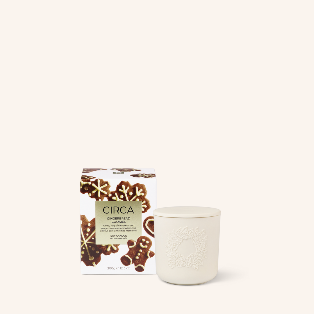 White ceramic candle with an embossed wreath and a lid. The candle packaging features gingerbread cookies and gingerbread men on a white background