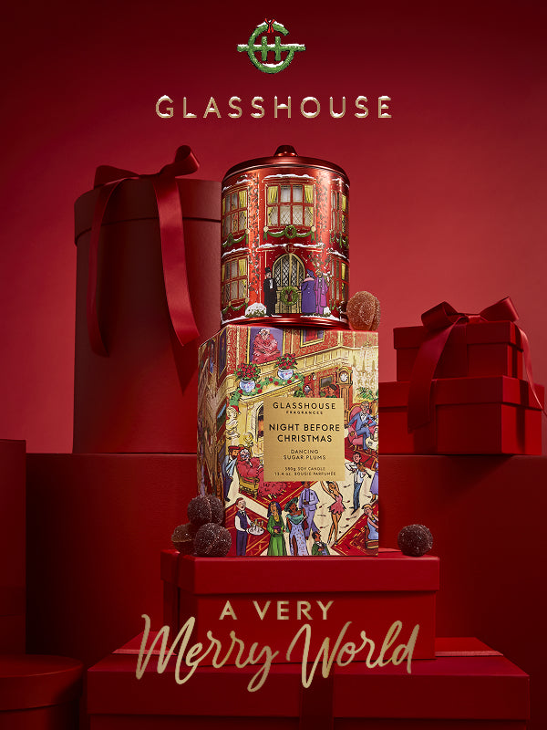 A festive product display for Glasshouse Cosmetics featuring a 'Night Before Christmas' limited edition makeup set. The set includes a cylindrical tin with a detailed red Christmas house illustration, a matching illustrated cardboard box, and decorative red gift boxes with ribbons in the background.